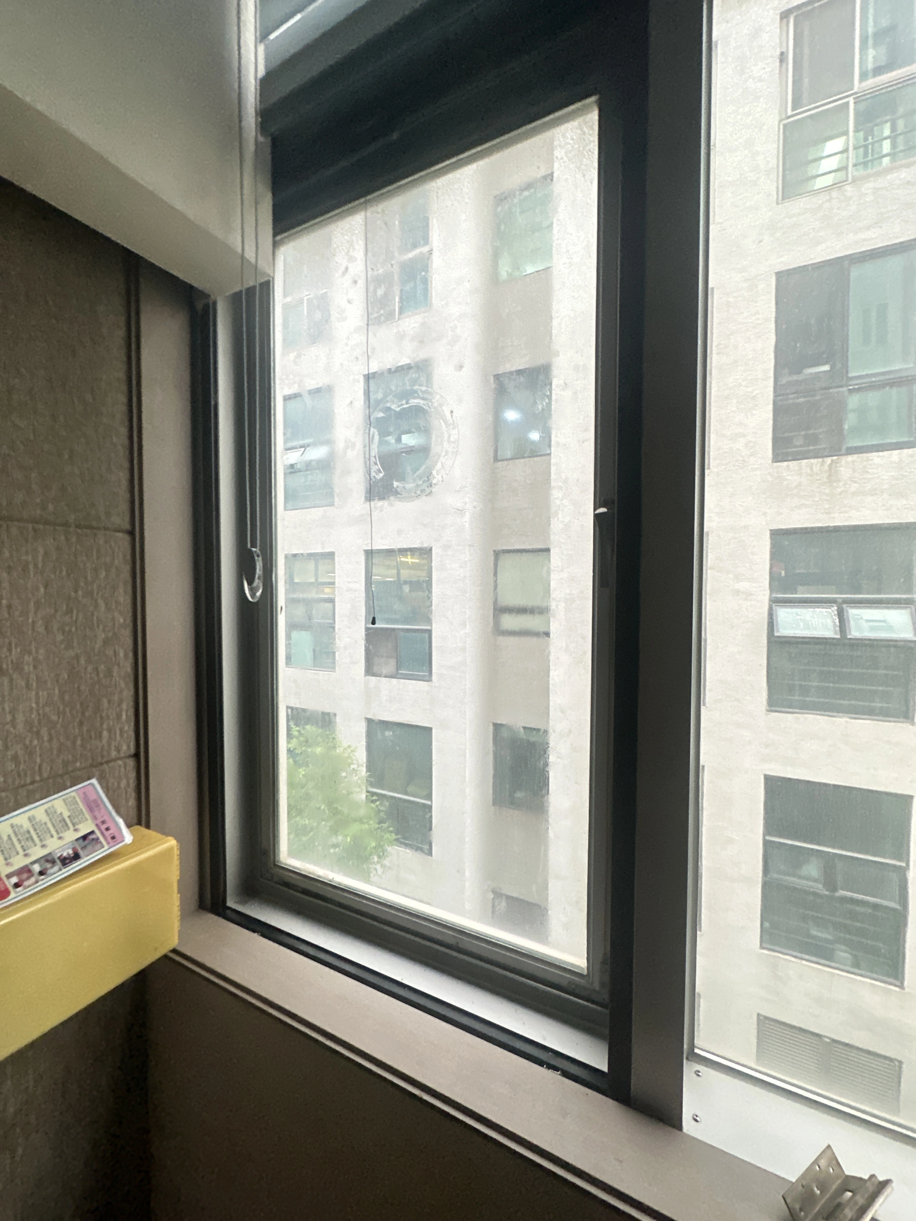 고층에서 열린 창문 사이로 보이는 도심 스카이라인과 노란 상자
