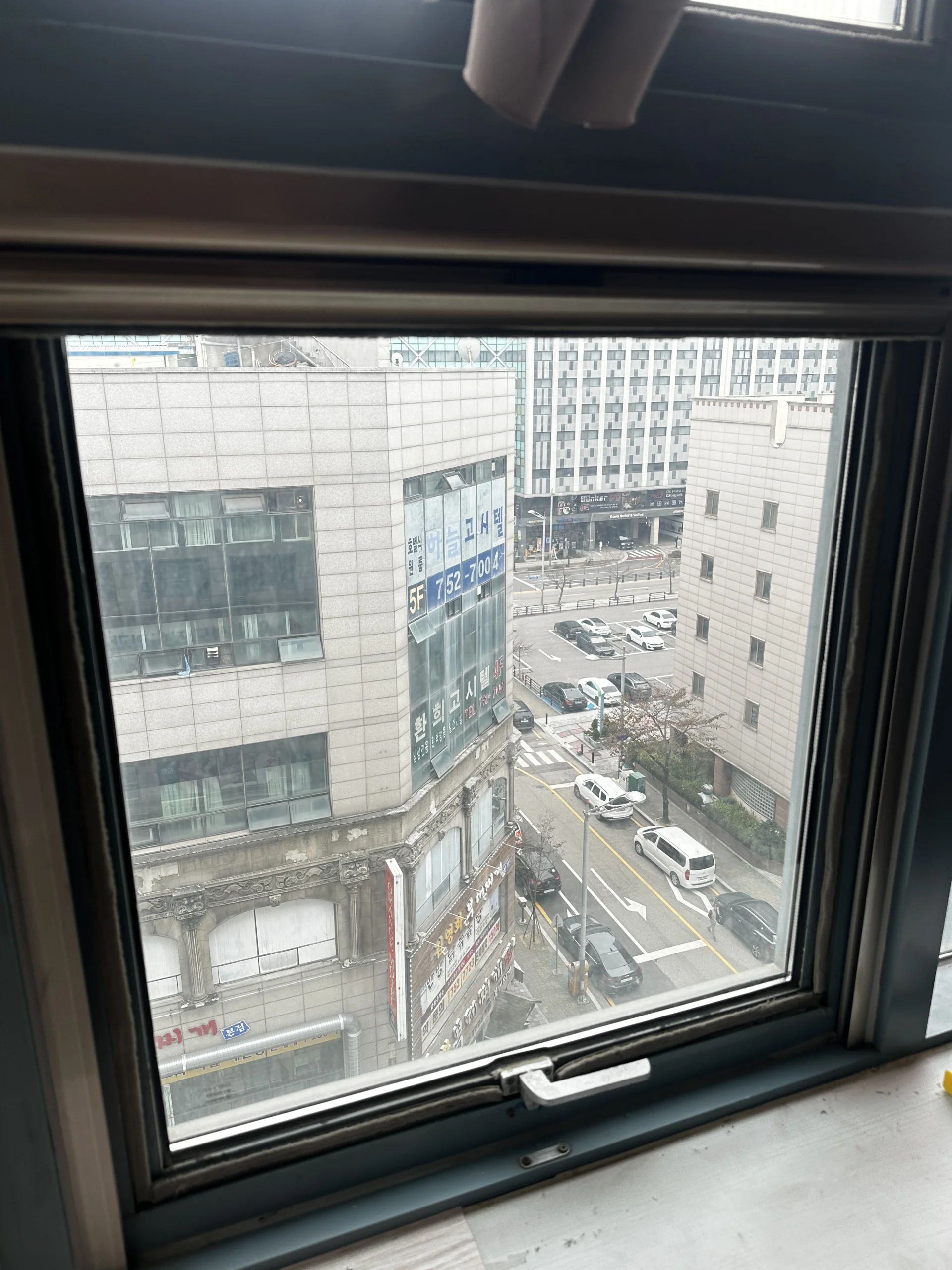 완전히 개방된 검은 프레임 창문 너머로 보이는 도심 빌딩